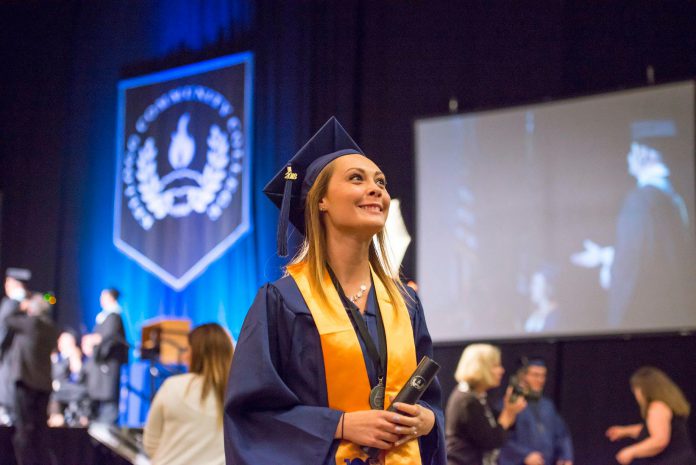 At graduation, a girl in cap and gown holds her diploma