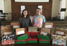 Two women standing behind festive shoe boxes, filled with various items.