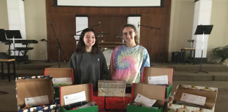 Two women standing behind festive shoe boxes, filled with various items.