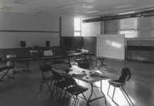 A black and white photo showing light falling through a window on a table in a classroom.