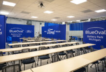 A training classroom featuring tables and chairs and blue walls with white Ford and BlueOval logos on them.